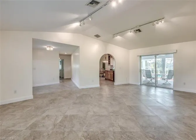 Empty room featuring light tile patterned flooring, vaulted ceiling, and track lighting