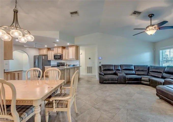 Dining area featuring light tile patterned floors, ceiling fan with notable chandelier, and lofted ceiling