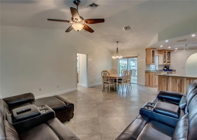 Living room featuring sink, vaulted ceiling, ceiling fan with notable chandelier, and light tile patterned floors