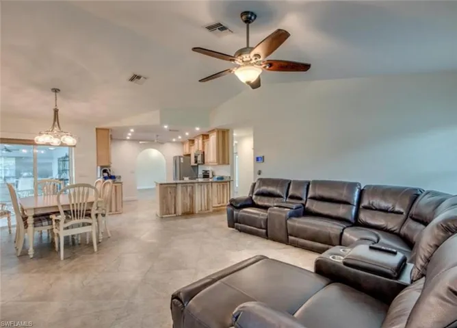 Living room featuring light tile patterned floors, ceiling fan with notable chandelier, and vaulted ceiling