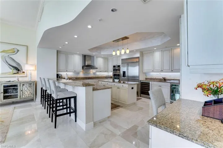 Kitchen featuring wall chimney range hood, a kitchen island, beverage cooler, appliances with stainless steel finishes, and crown molding