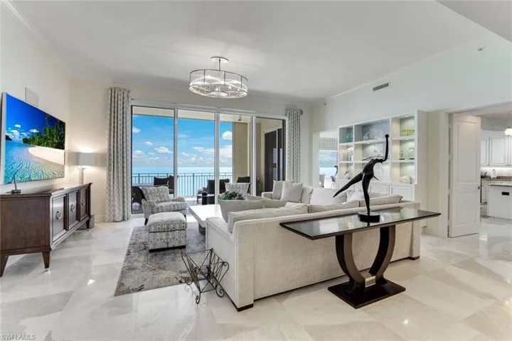 Living area with crown molding, a chandelier, a water view, and light marble finish floors
