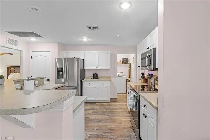 Kitchen with white cabinets, stainless steel appliances, washer / dryer, and light hardwood / wood-style flooring