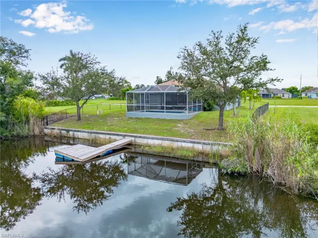 View of dock with a water view, glass enclosure, and a yard
