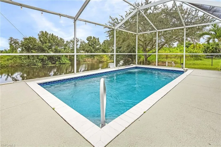 View of pool with glass enclosure, a water view, and a patio area