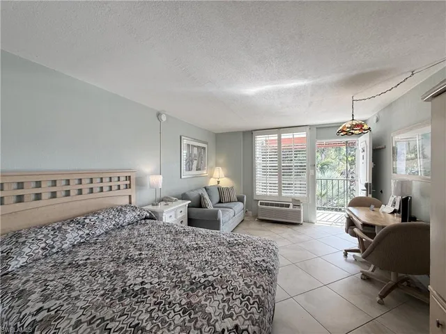 Bedroom featuring access to exterior, a desk, a textured ceiling, light tile patterned floors, and an AC wall unit