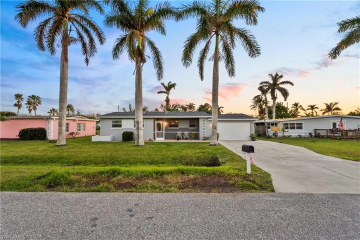 Single-story residence featuring a concrete driveway, attached garage, and mature palm trees situated on a grassy lot