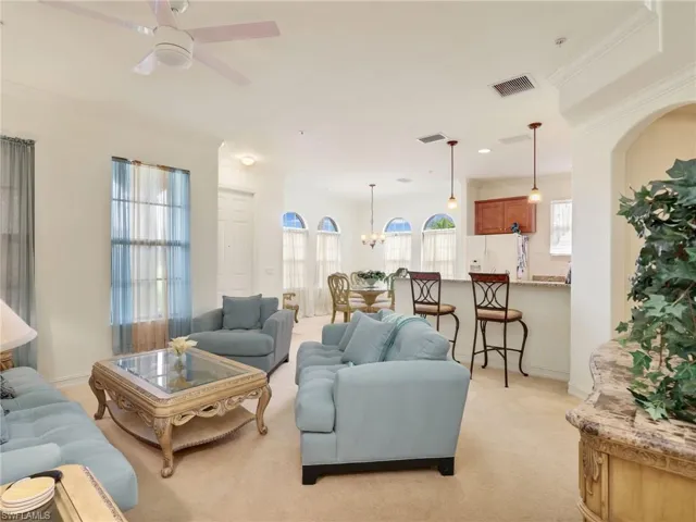 Living area featuring light carpet, ornamental molding, healthy amount of natural light, a chandelier, and ceiling fan