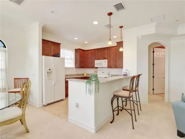 Kitchen featuring arched walkways, light colored carpet, white appliances, hanging light fixtures, and a kitchen bar