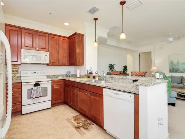 Kitchen with white appliances, hanging light fixtures, light stone counters, a peninsula, and ornamental molding