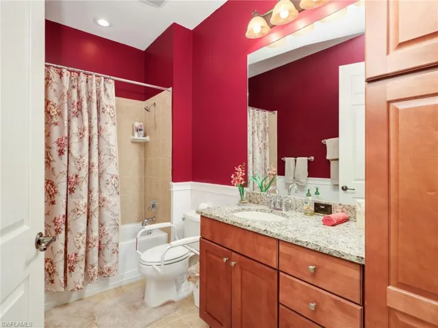 Full bath featuring shower / tub combo with curtain, vanity, wainscoting, and light tile patterned floors