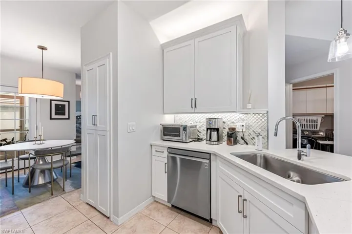 Kitchen with light tile patterned flooring, white cabinetry, sink, hanging light fixtures, and stainless steel dishwasher