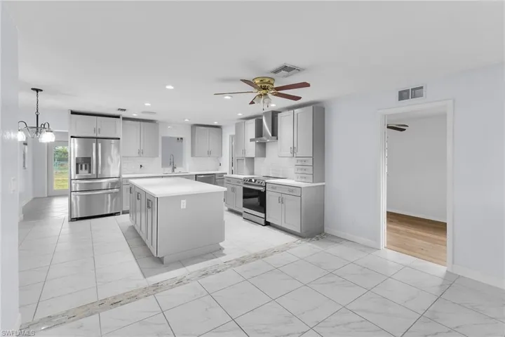 Kitchen with light marble finish flooring, stainless steel appliances, light countertops, backsplash, and a kitchen island