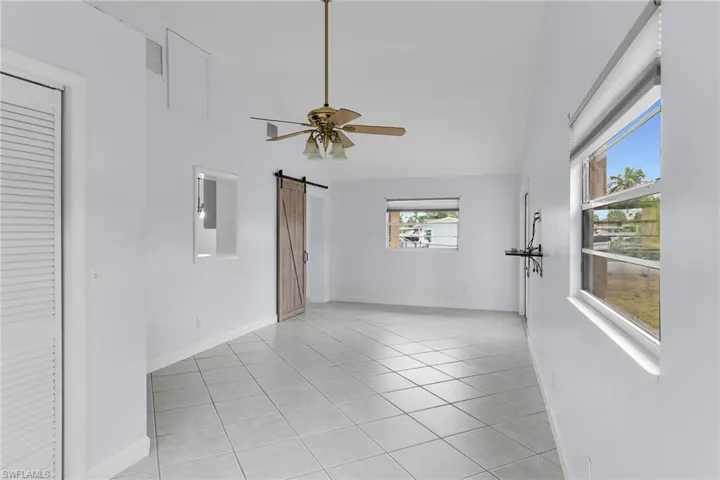 Unfurnished room featuring a barn door, light tile patterned flooring, ceiling fan, and high vaulted ceiling
