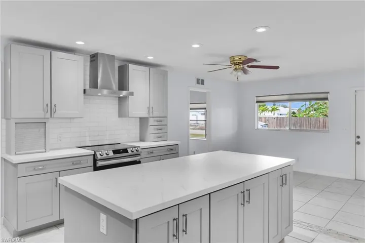 Kitchen with wall chimney range hood, electric stove, a kitchen island, backsplash, and recessed lighting