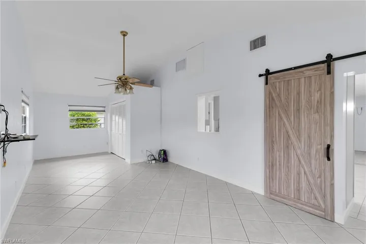 Unfurnished living room with high vaulted ceiling, a ceiling fan, a barn door, and light tile patterned floors