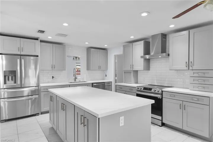 Kitchen with stainless steel appliances, a ceiling fan, gray cabinets, wall chimney exhaust hood, and light marble finish flooring