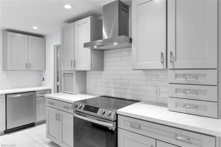 Kitchen with stainless steel appliances, wall chimney exhaust hood, light marble finish flooring, light stone counters, and decorative backsplash