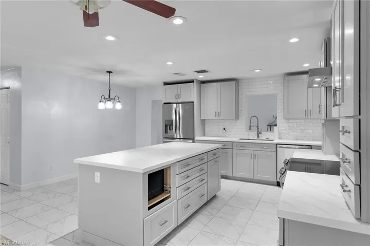 Kitchen with light marble finish floors, recessed lighting, light stone counters, stainless steel fridge with ice dispenser, and a center island