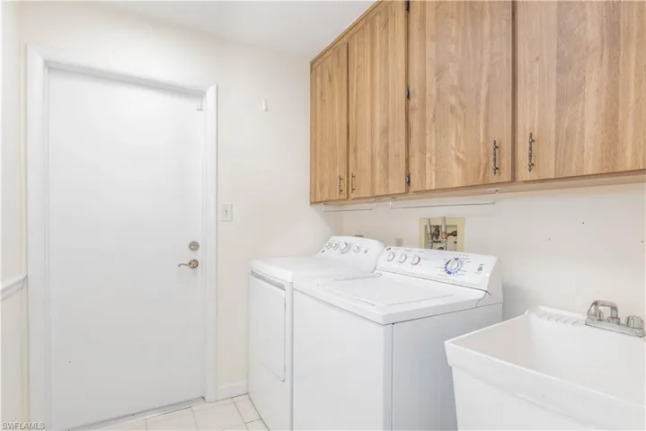 Laundry room with sink, light tile patterned floors, washing machine and dryer, and cabinets