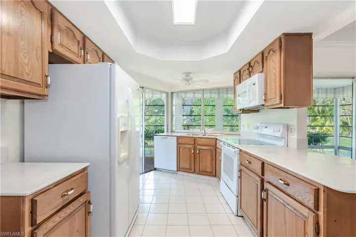 Kitchen featuring a raised ceiling, a healthy amount of sunlight, light tile patterned floors, and white appliances