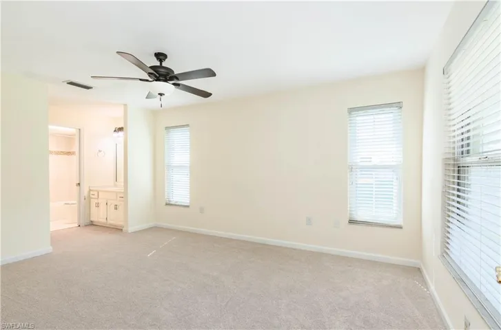 Unfurnished bedroom with ceiling fan, ensuite bathroom, and light carpet