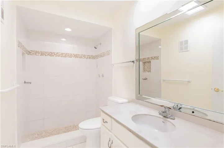 Bathroom featuring tiled shower, vanity, and toilet