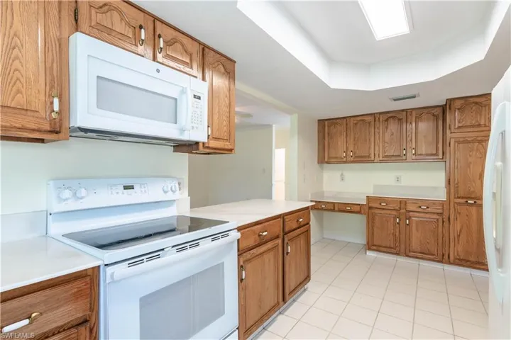 Kitchen featuring light tile patterned flooring, white appliances, and a tray ceiling
