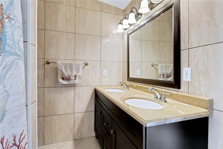 Full bath featuring double vanity, tile walls, and light tile patterned flooring
