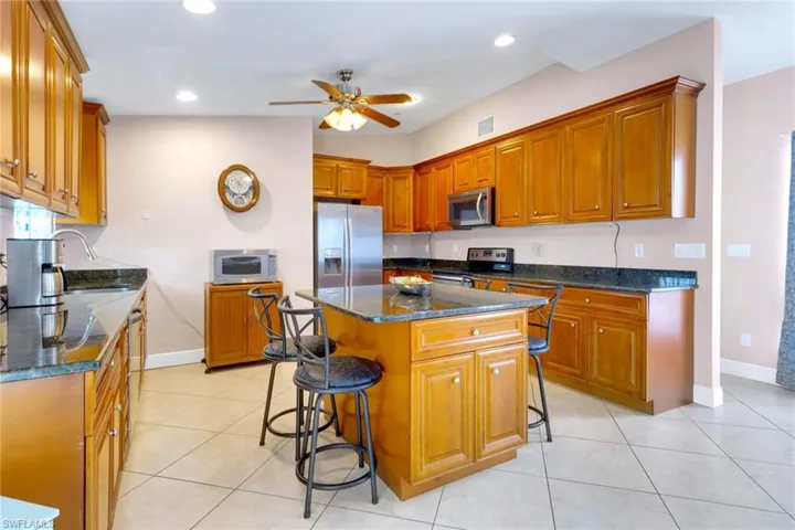 Kitchen with a kitchen breakfast bar, dark stone countertops, brown cabinets, light tile patterned floors, and appliances with stainless steel finishes