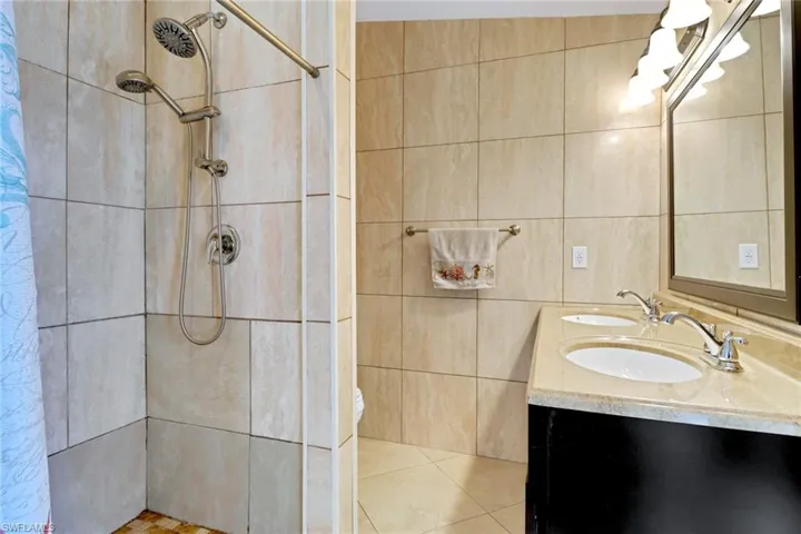 Full bath with double vanity, a shower stall, tile walls, and tile patterned floors