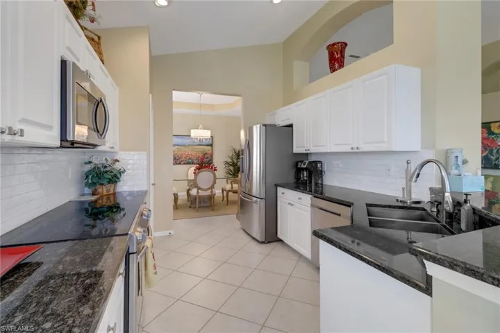 Kitchen featuring backsplash, white cabinetry, dark stone countertops, light tile patterned flooring, and stainless steel appliances
