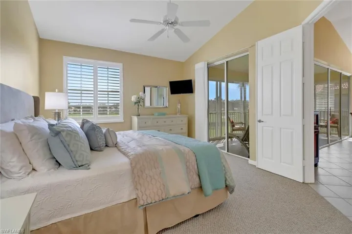Tiled bedroom with ceiling fan, vaulted ceiling, and access to exterior