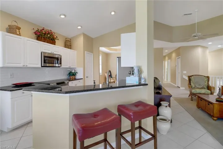Kitchen with decorative backsplash, white cabinets, kitchen peninsula, ceiling fan, and light tile patterned flooring