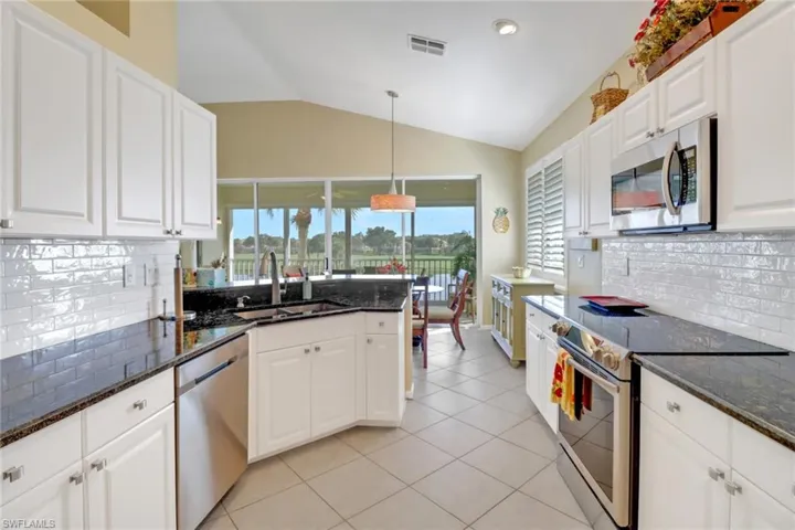 Kitchen with sink, dark stone countertops, appliances with stainless steel finishes, and lofted ceiling