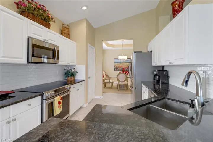 Kitchen with backsplash, stainless steel appliances, light tile patterned flooring, and white cabinets