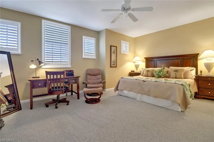 Carpeted bedroom with ceiling fan and multiple windows