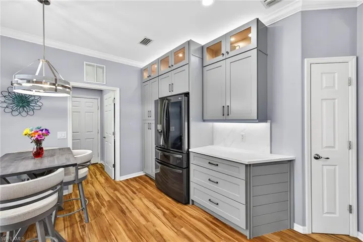 Kitchen featuring crown molding, gray cabinetry, refrigerator with ice dispenser, pendant lighting, and glass insert cabinets