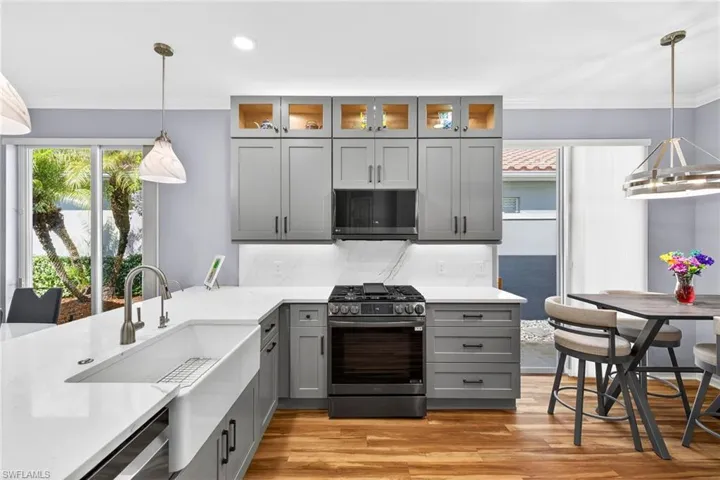 Kitchen featuring decorative light fixtures, gray cabinetry, gas range, glass insert cabinets, and light stone counters
