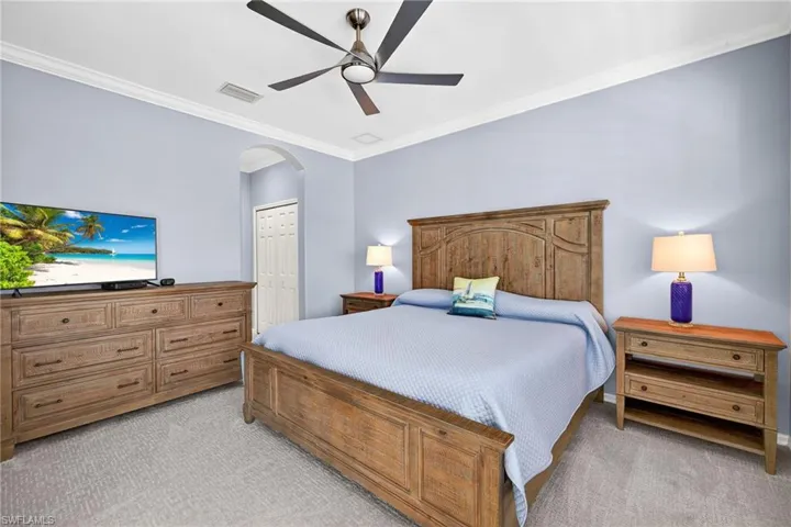 Bedroom featuring ornamental molding, light carpet, a closet, a ceiling fan, and arched walkways