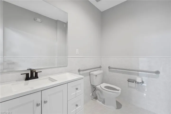 Bathroom with tile walls, vanity, a wainscoted wall, and light tile patterned floors