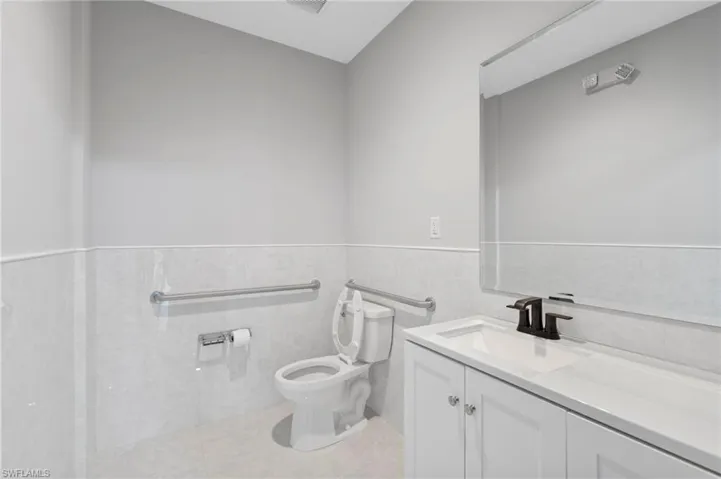 Half bath with vanity, tile walls, a wainscoted wall, and light tile patterned flooring