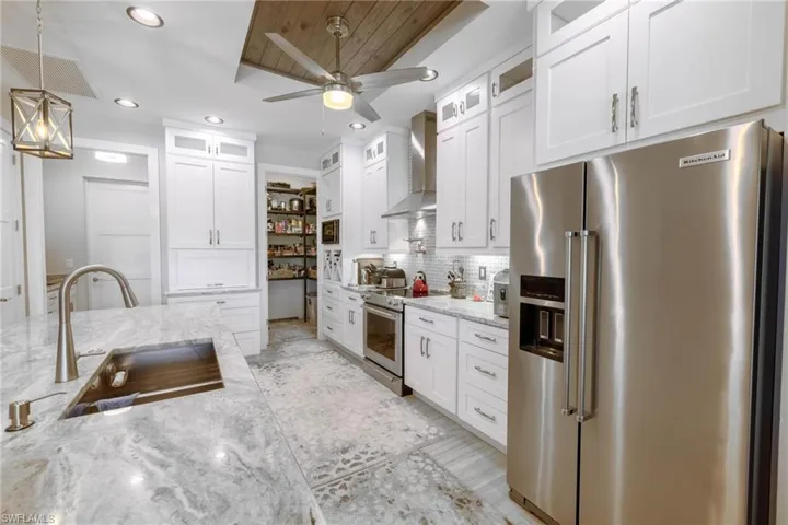 Kitchen featuring stainless steel appliances, wall chimney range hood, sink, and white cabinets
