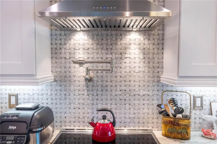 Kitchen featuring wall chimney exhaust hood, white cabinets, light stone counters, and backsplash