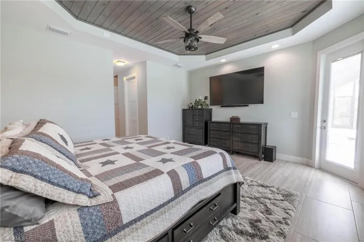 Tiled bedroom featuring ceiling fan, a raised ceiling, and wooden ceiling