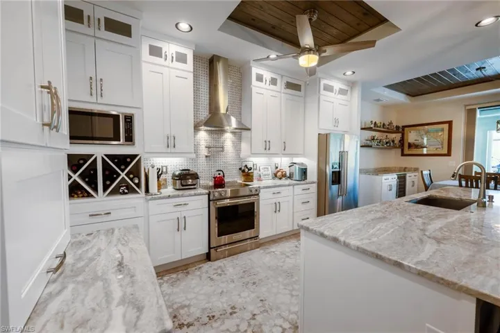 Kitchen featuring light stone countertops, sink, white cabinetry, stainless steel appliances, and wall chimney exhaust hood