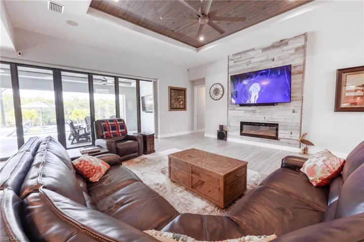 Living room featuring ceiling fan, a fireplace, wooden ceiling, and a raised ceiling