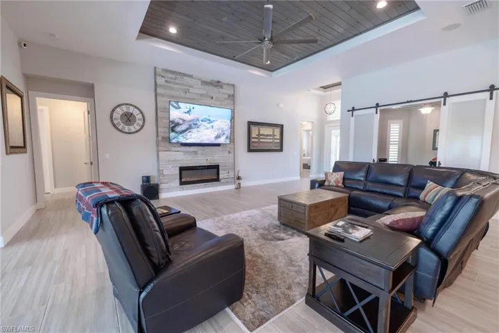 Living room with ceiling fan, a barn door, a tray ceiling, light hardwood / wood-style flooring, and a fireplace