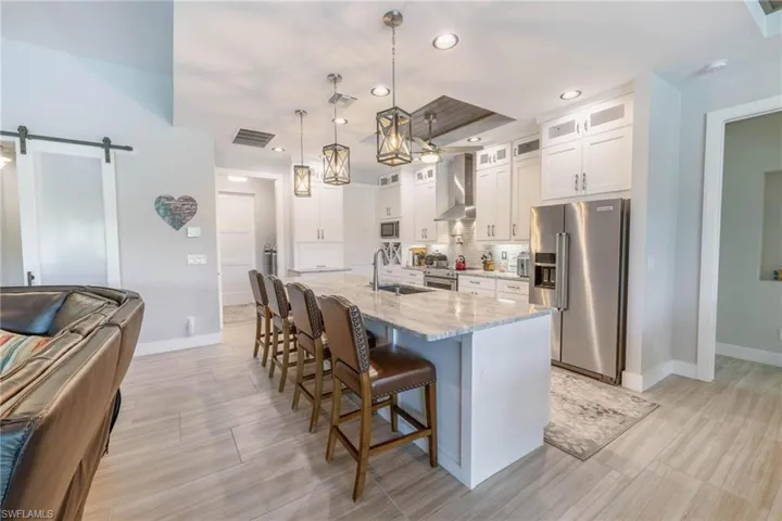 Kitchen featuring wall chimney range hood, sink, a barn door, decorative light fixtures, and appliances with stainless steel finishes