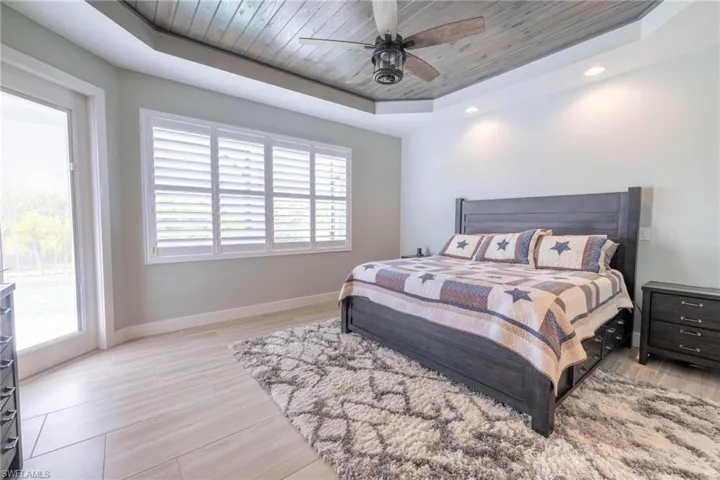 Bedroom with a raised ceiling, multiple windows, and ceiling fan